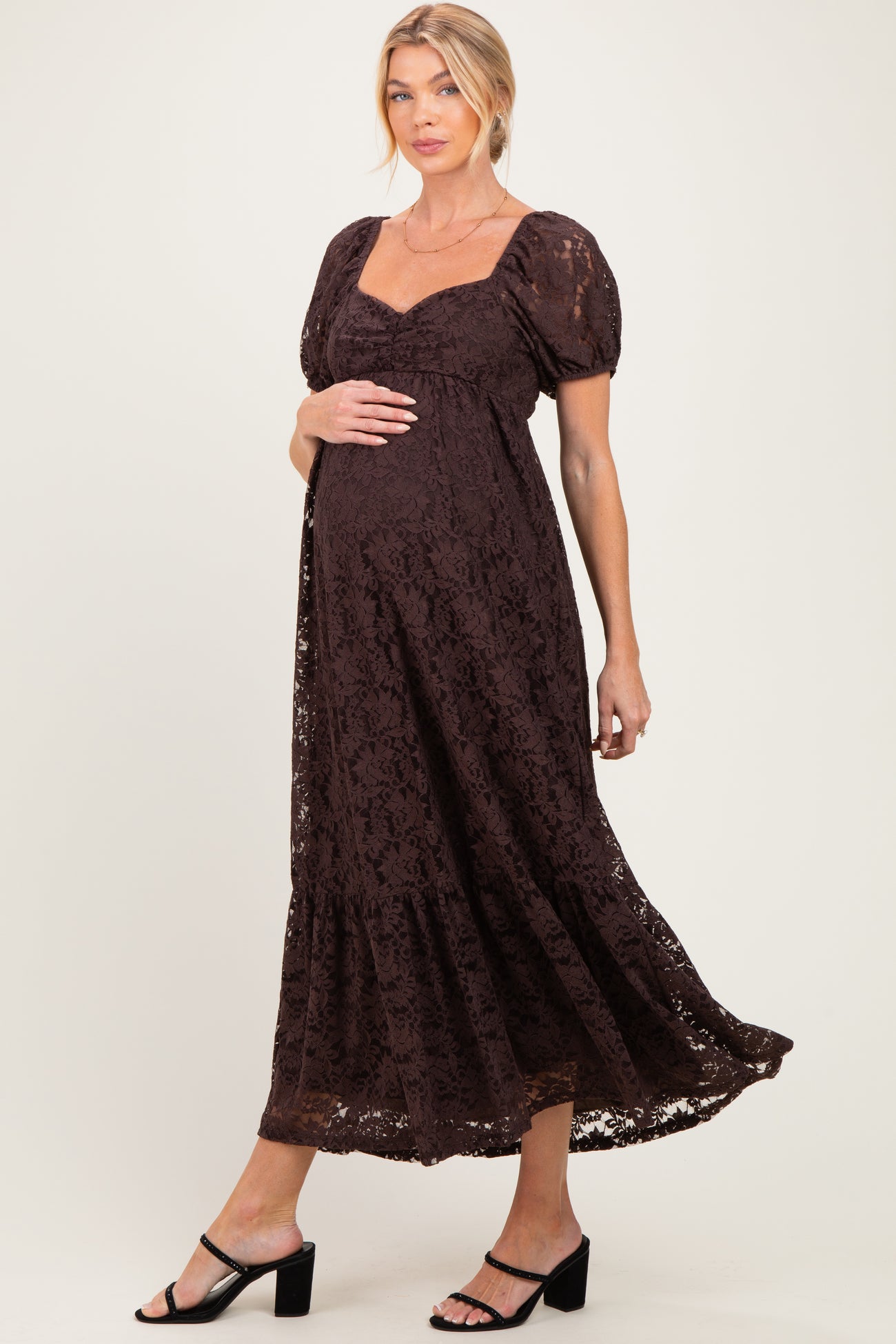 woman wearing a brown lace maternity dress with puff sleeves and a flowing skirt, showcasing her baby bump