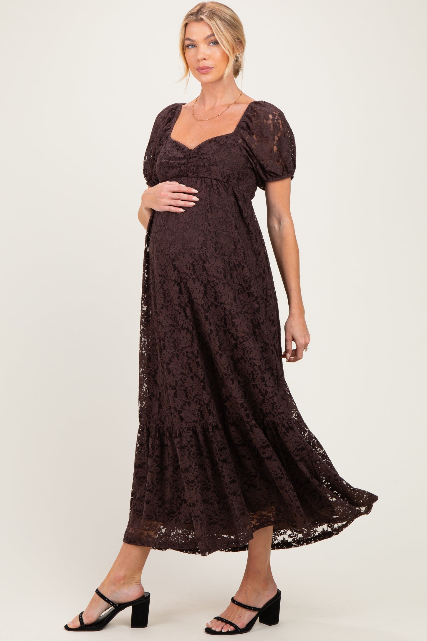 woman wearing a brown lace maternity dress with puff sleeves and a flowing skirt, showcasing her baby bump