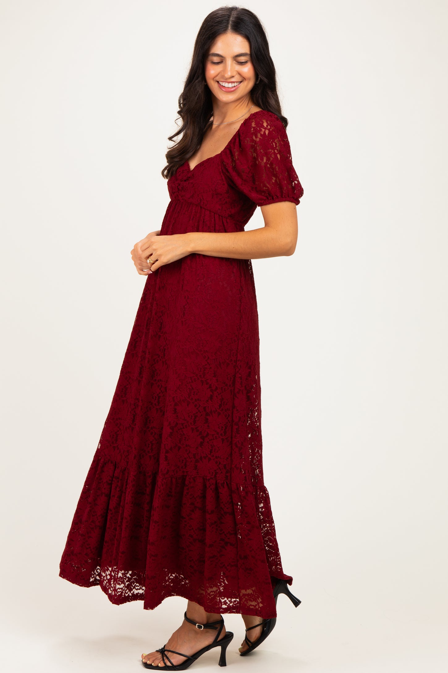 woman wearing a burgundy lace maxi dress with puff sleeves and a tiered hem, smiling to the side