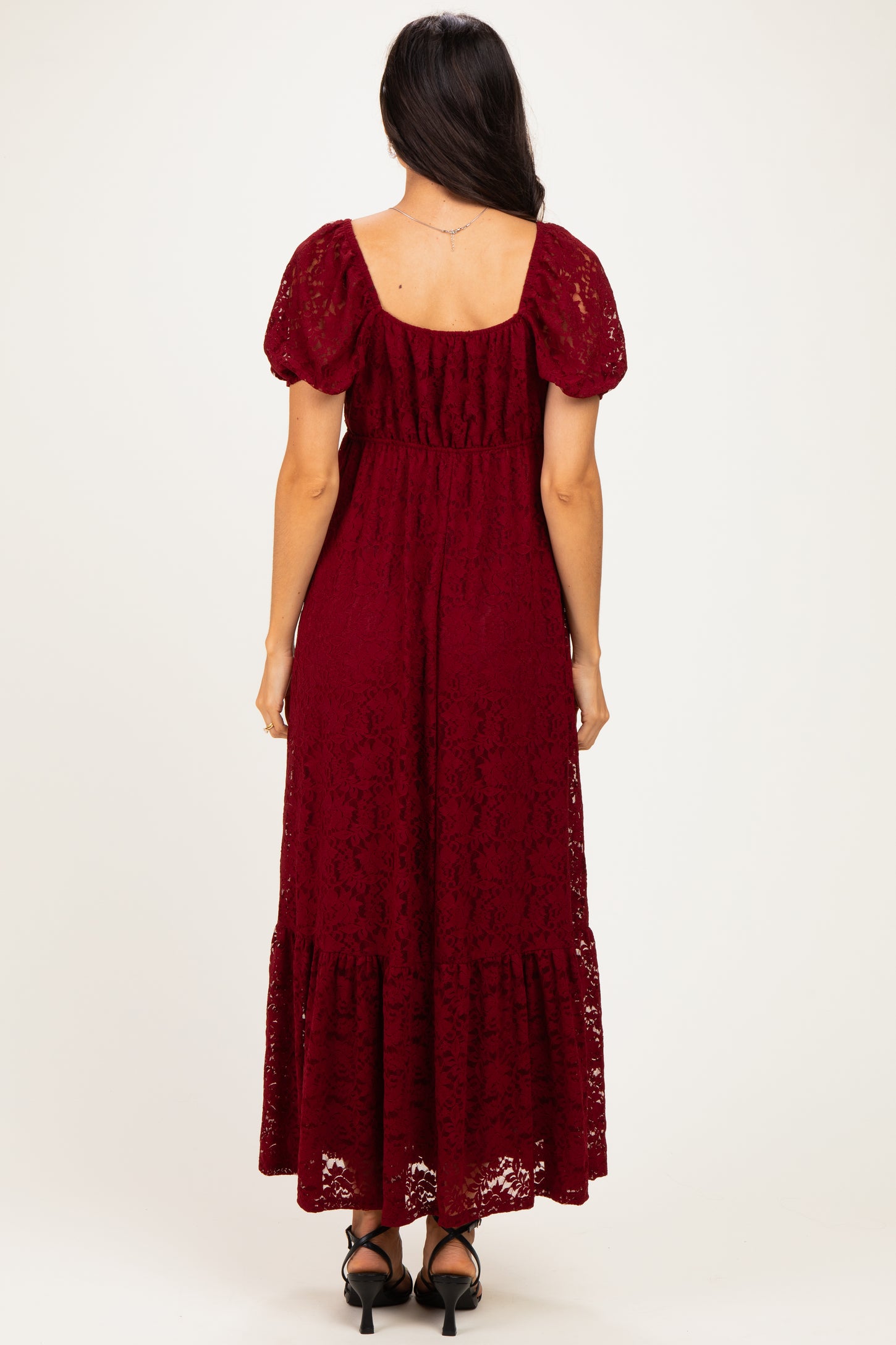 woman wearing a burgundy lace maxi dress with short puff sleeves and a tiered hem, seen from the back