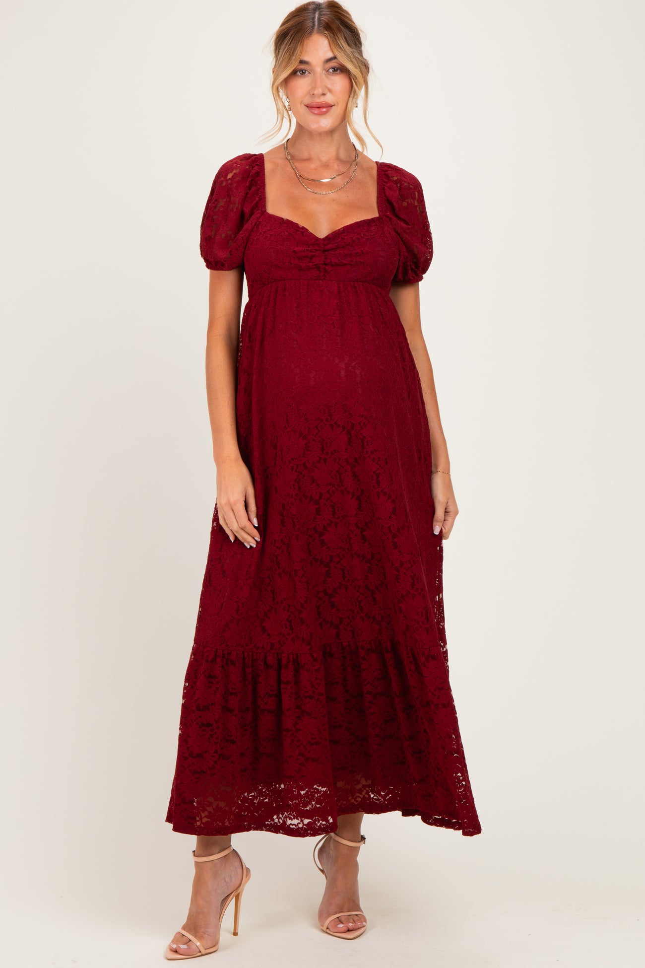 woman wearing a burgundy lace maternity maxi dress with puff sleeves and a gathered bodice, showing her baby bump