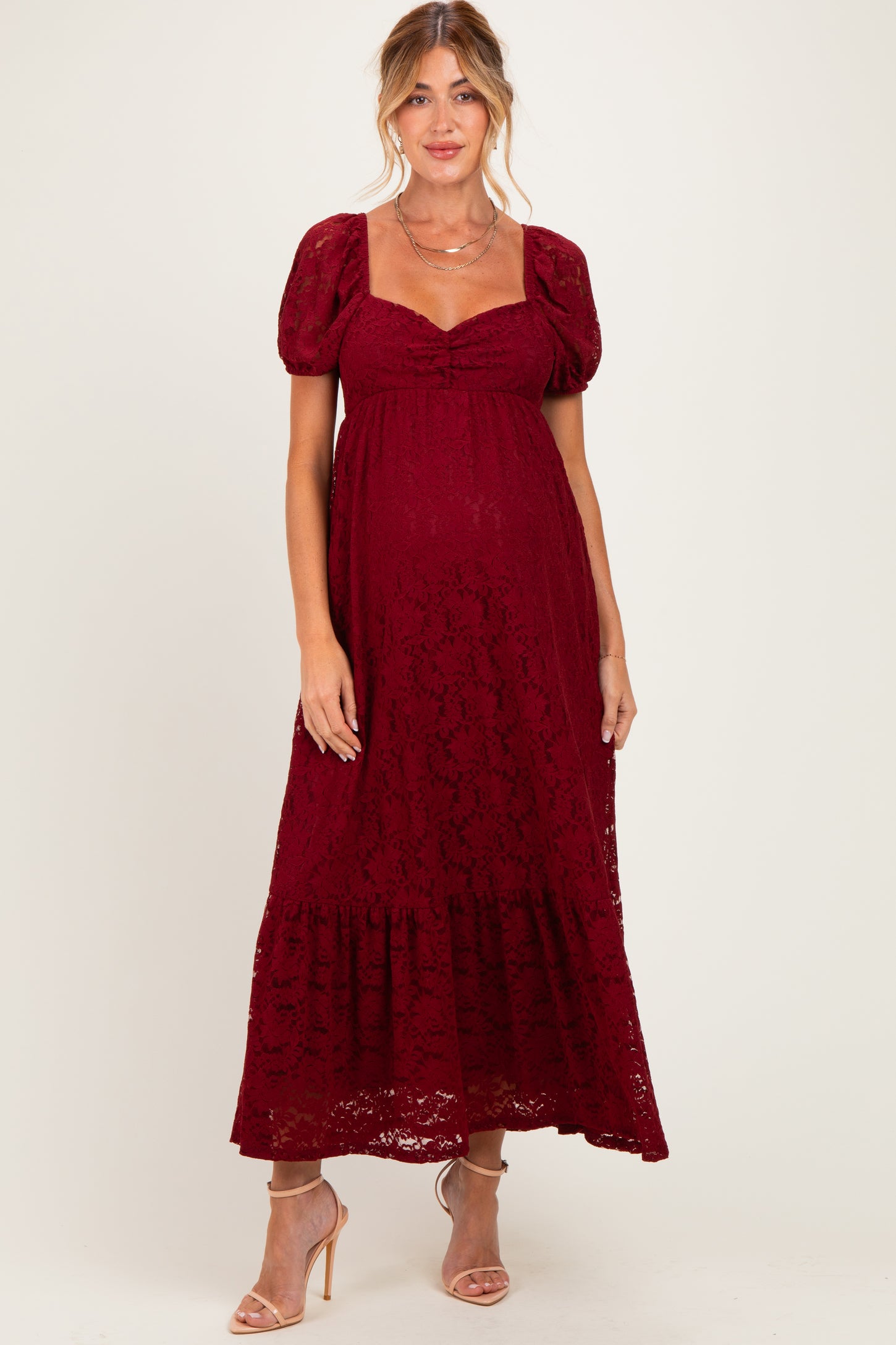 woman wearing a burgundy lace maternity maxi dress with puff sleeves and a gathered bodice, showing her baby bump