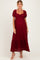 woman wearing a burgundy lace maternity maxi dress with puff sleeves and a gathered bodice, showing her baby bump