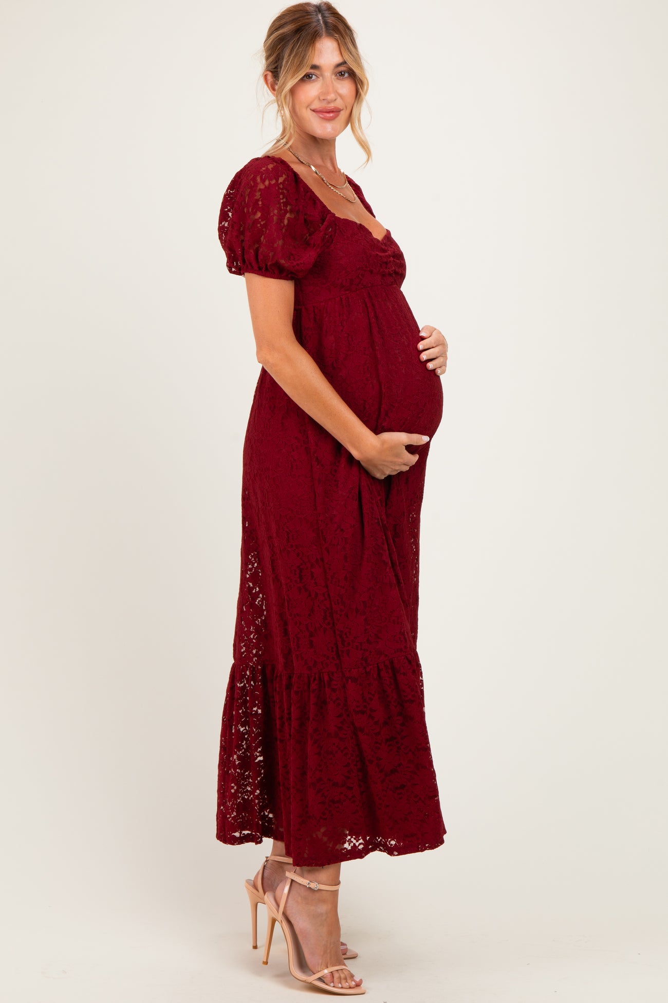 woman wearing a burgundy lace maternity maxi dress and holding her baby bump