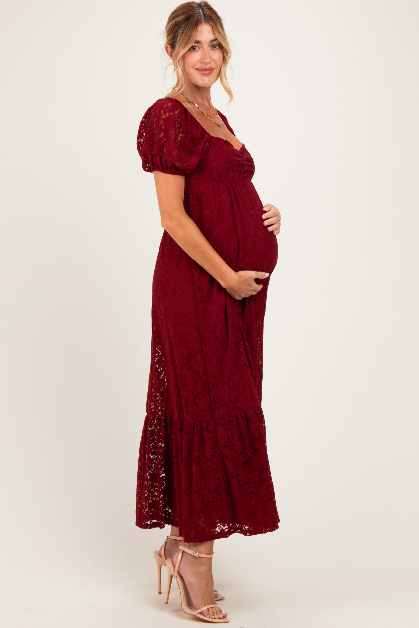 woman wearing a burgundy lace maternity maxi dress and holding her baby bump