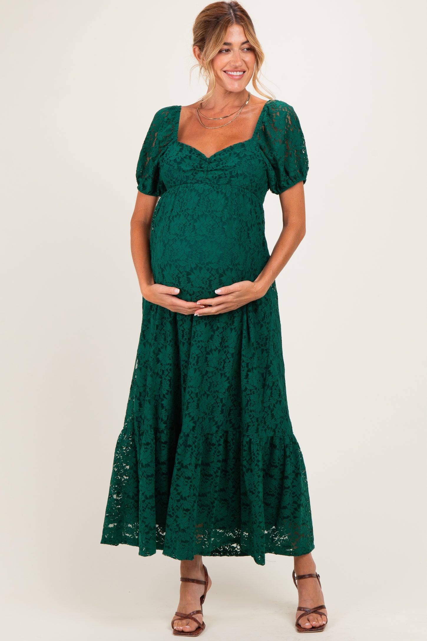 woman wearing a dark green lace maternity dress with puff sleeves and a flowing skirt, holding her baby bump