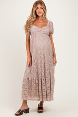 woman wearing a light brown lace maternity dress with puff sleeves and a tiered hem, showing her baby bump