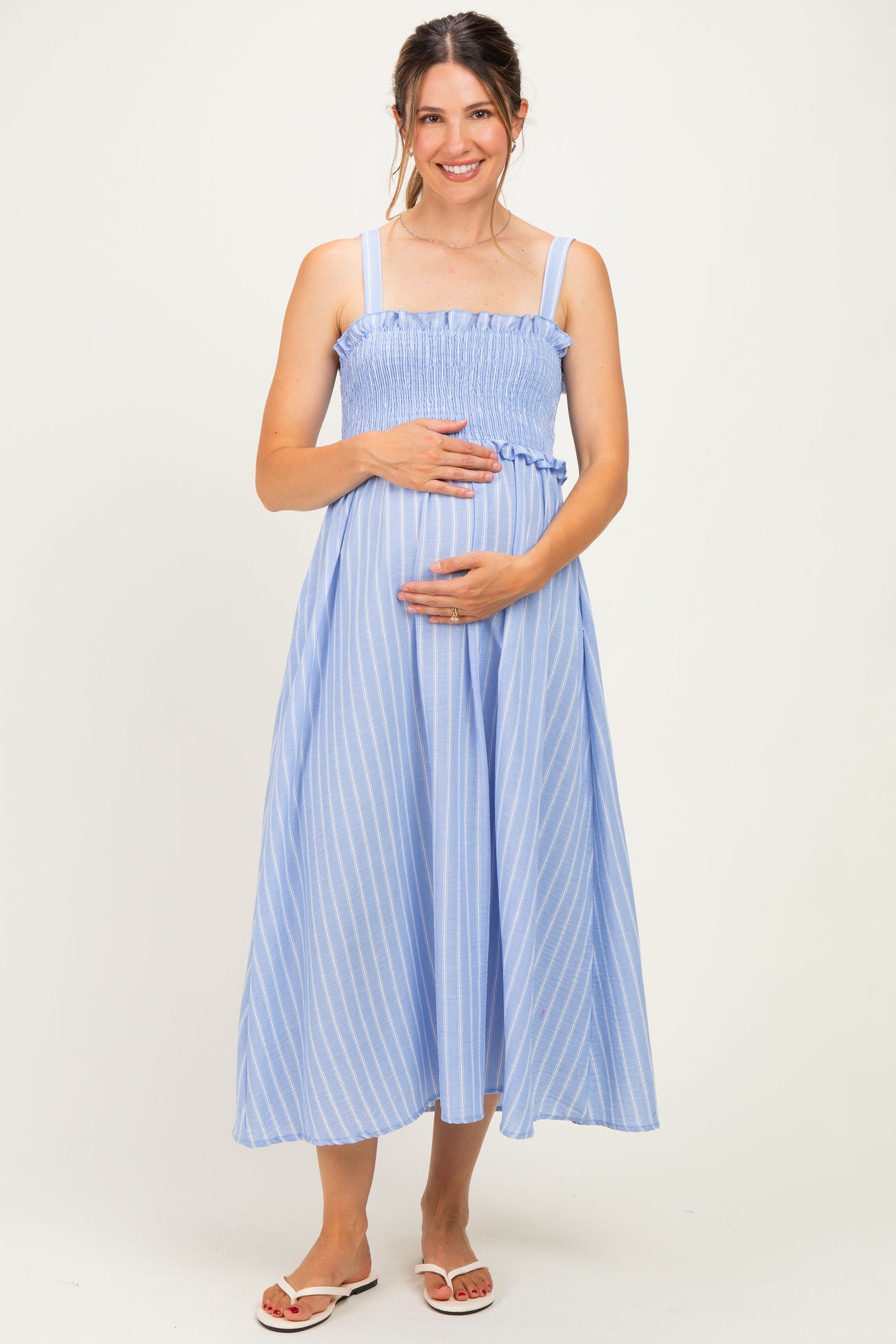 woman wearing a blue and white striped maternity dress with smocked detailing and holding her baby bump