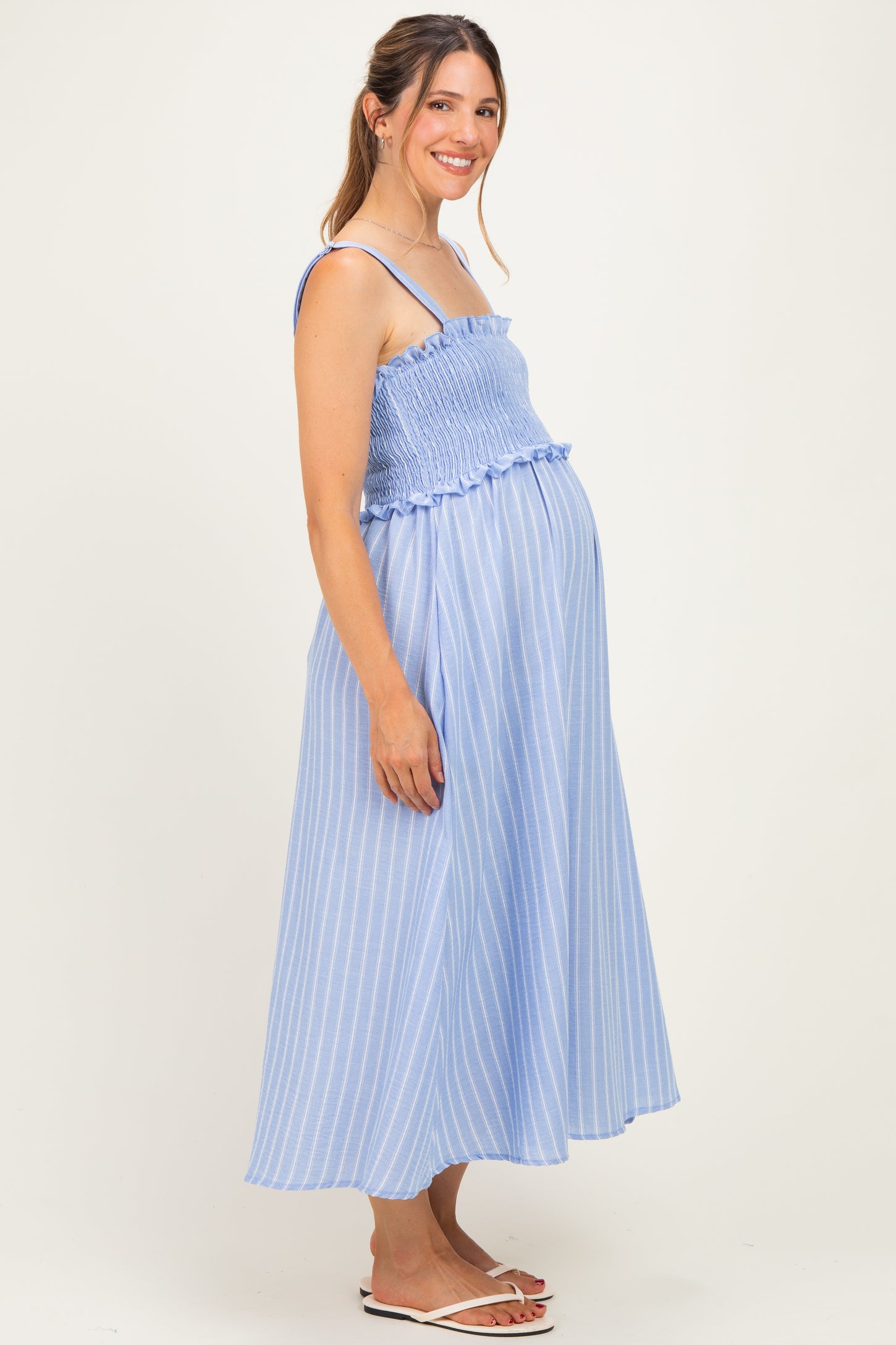 woman wearing a light blue striped maternity maxi dress with smocked bodice and ruffle detail, showcasing her baby bump