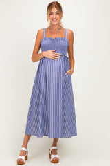 woman wearing a blue and white striped maternity dress with smocked bodice and pockets, holding her baby bump