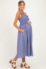 woman wearing a blue and white striped maternity dress with a smocked bodice and pockets, showing her baby bump
