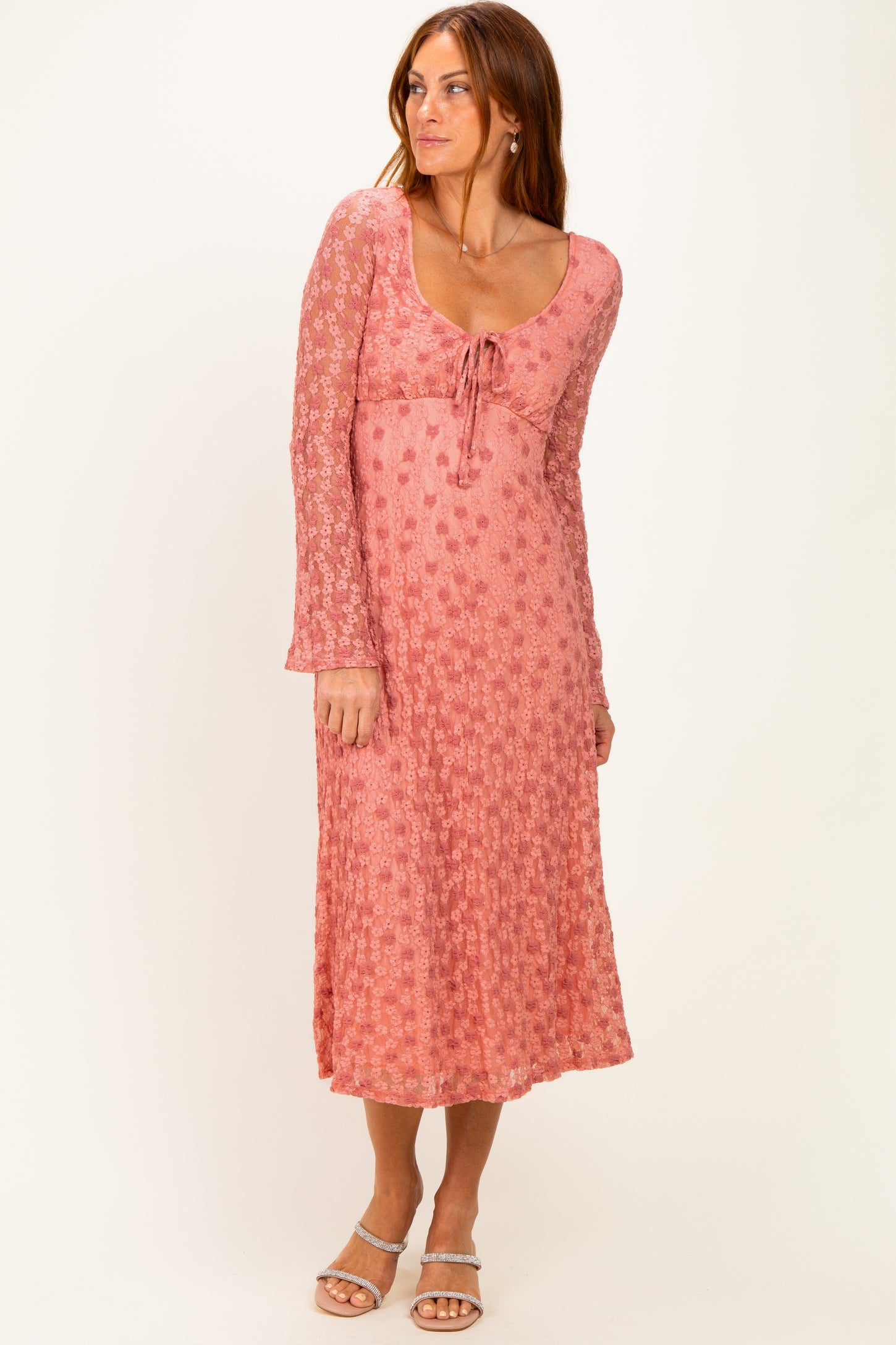 woman wearing a pink floral long sleeve midi dress with a tie detail at the neckline and a flowing skirt