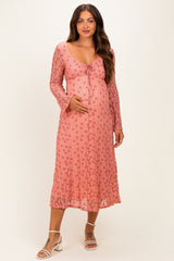 woman wearing a pink floral maternity dress with long sleeves and a tie front, holding her baby bump