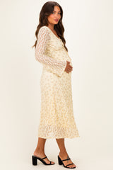 woman wearing a light yellow embroidered maternity dress with long lace sleeves and holding her baby bump