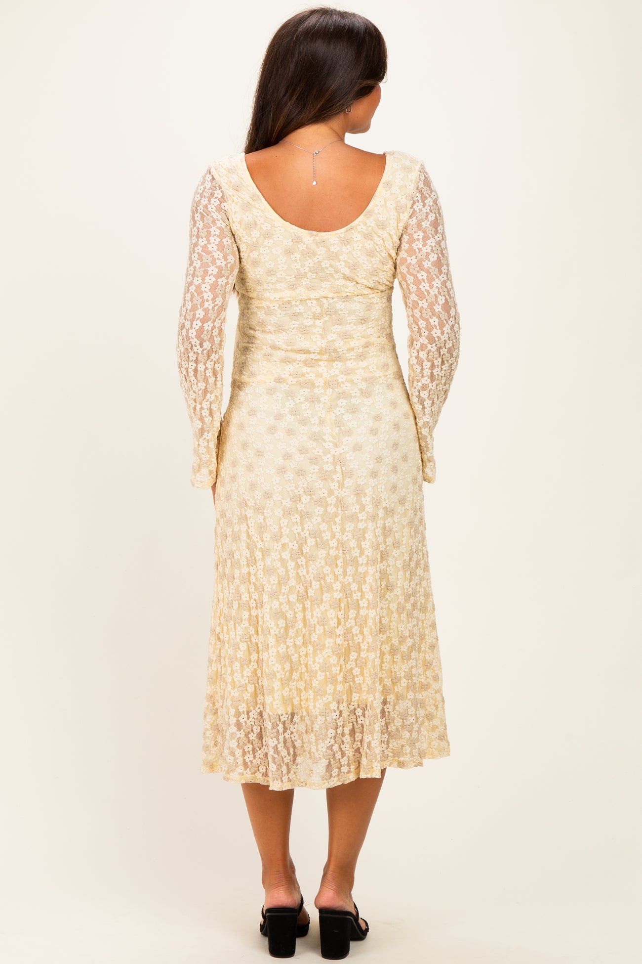 woman wearing a cream floral lace maternity dress with long sleeves and a flowing skirt from a rear view
