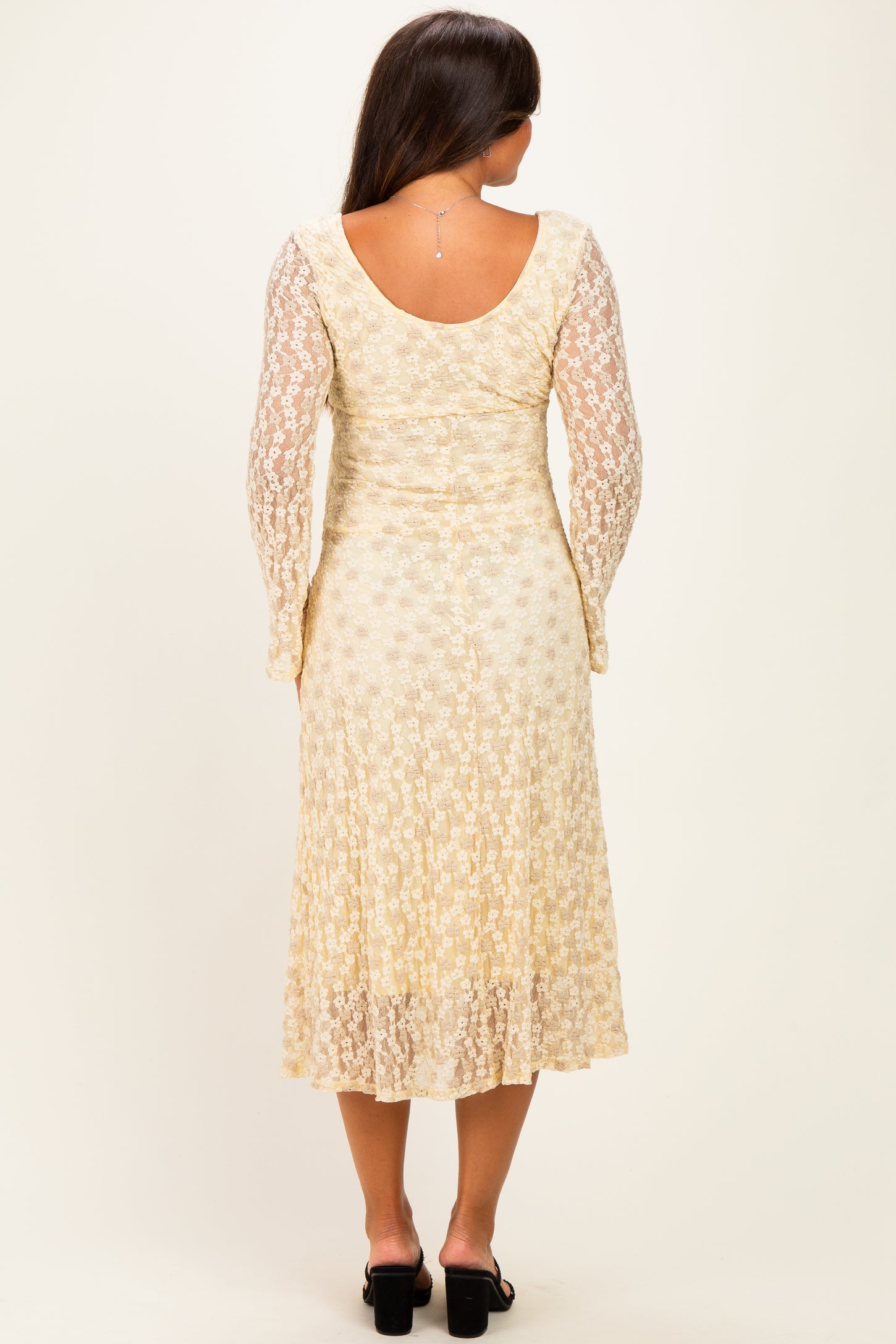 woman wearing a cream floral lace maternity dress with long sleeves and a flowing skirt from a rear view