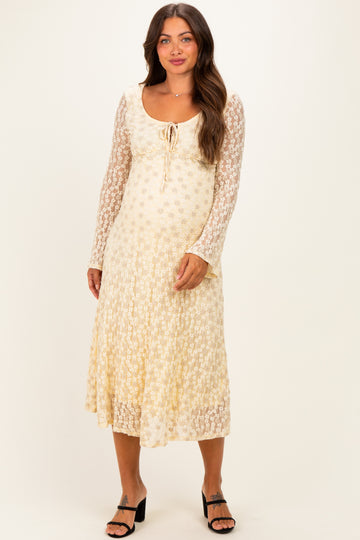 woman wearing a cream floral lace maternity dress with long sleeves and a tie detail at the neckline, showcasing her baby bump