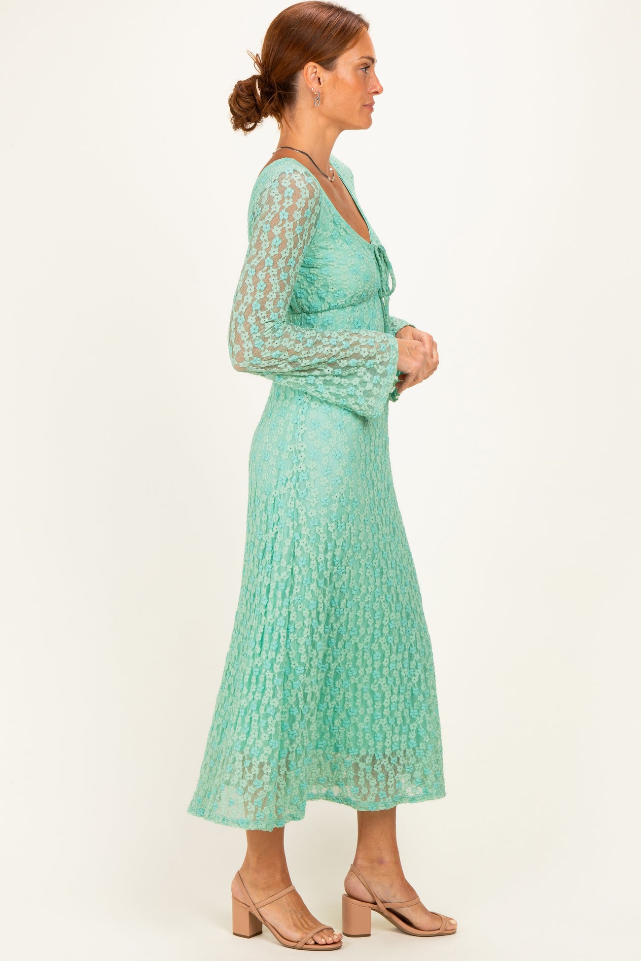 woman wearing a mint green lace dress with long sleeves and a flared skirt, standing in profile