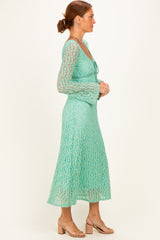 woman wearing a mint green lace dress with long sleeves and a flared skirt, standing in profile