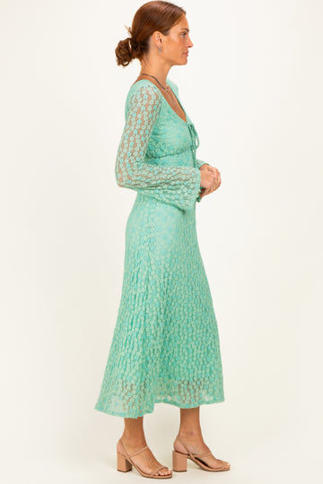 woman wearing a mint green lace dress with long sleeves and a flared skirt, standing in profile