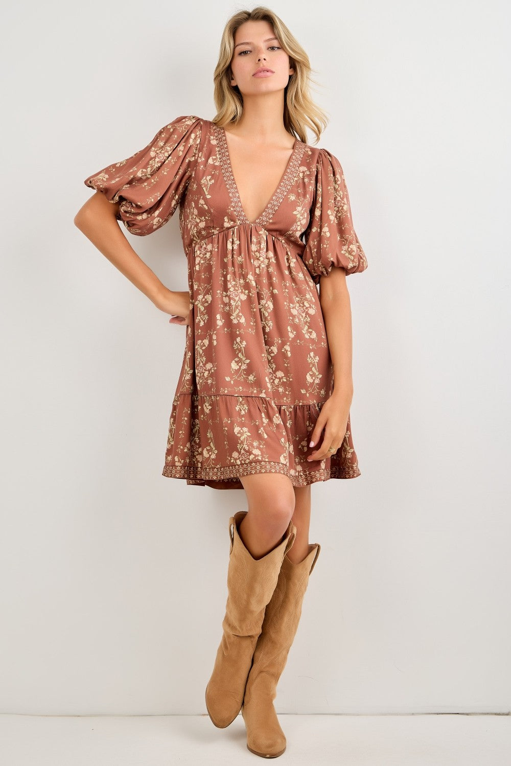 woman wearing a brown floral puff sleeve dress with a deep v-neck and tiered hem, paired with tan knee-high boots