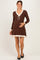 woman wearing a brown knit maternity dress with a v-neck and cream ruffle hem, holding her baby bump