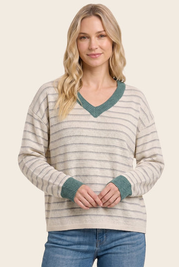 woman wearing a cream striped sweater with a v-neck and teal trim, styled with blue jeans