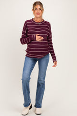 woman wearing a burgundy striped maternity sweater and blue jeans, holding her baby bump