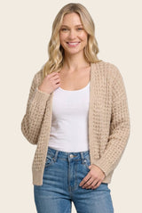 woman wearing a beige knitted cardigan over a white top and blue jeans, smiling at the camera
