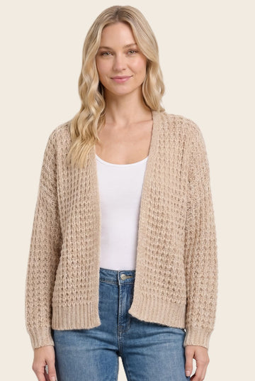 woman wearing a beige knitted cardigan over a white top and blue jeans