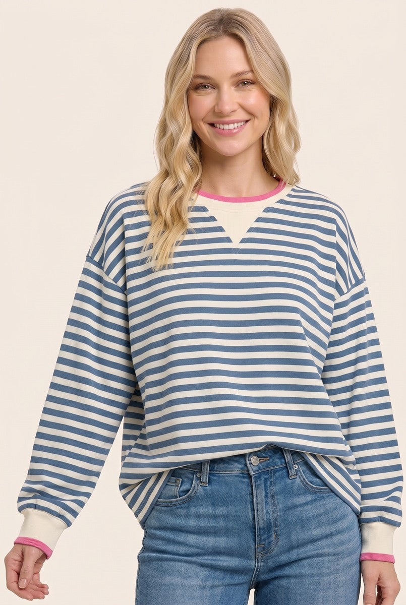 woman wearing a striped blue and white oversized sweatshirt with pink and white trim, smiling while posing