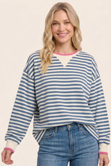 woman wearing a striped blue and white oversized sweatshirt with pink and white trim, smiling while posing