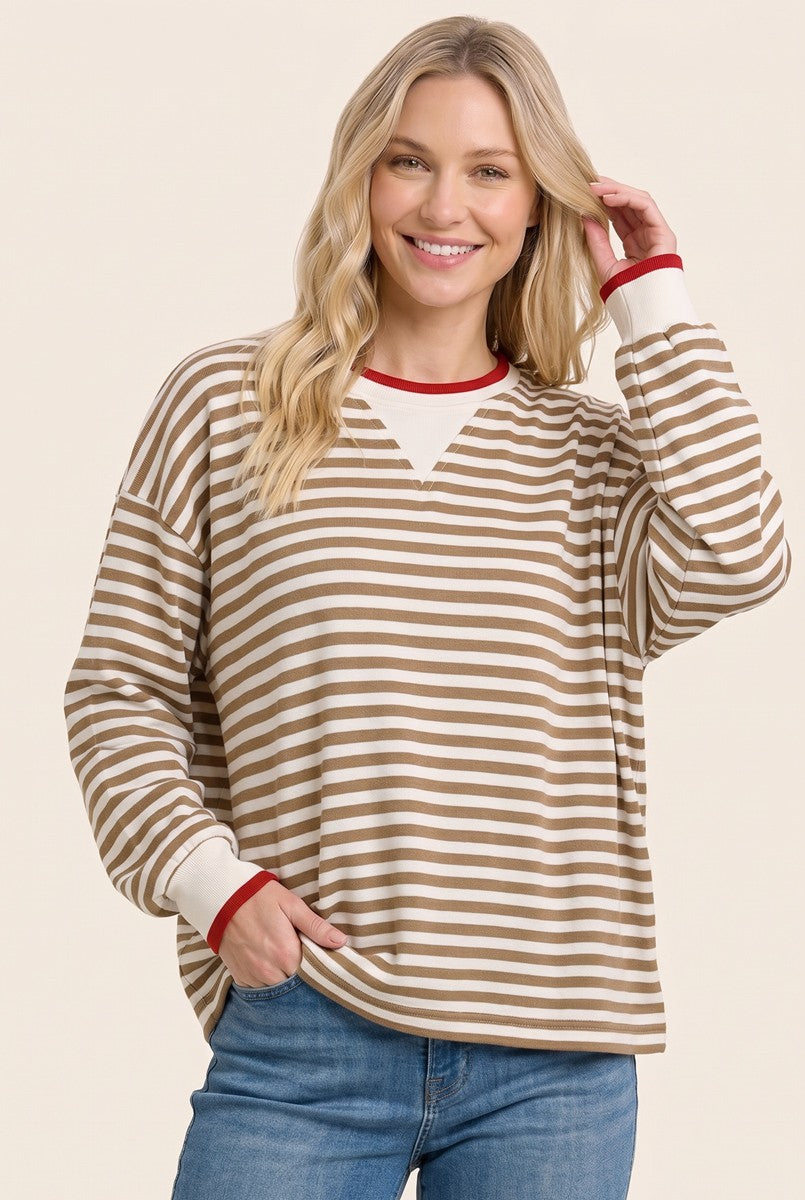 woman wearing a brown and white striped long sleeve top with red collar and cuffs, smiling while posing