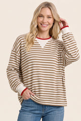 woman wearing a brown and white striped long sleeve top with red collar and cuffs, smiling while posing