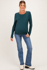 woman wearing a teal long sleeve maternity top and blue jeans, showcasing her baby bump