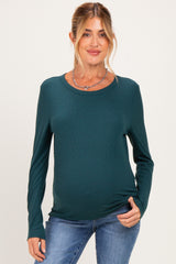 woman wearing a dark teal long sleeve maternity top and showing her baby bump while smiling