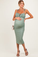 woman wearing a sage green maternity dress with adjustable straps and a gathered bodice, showcasing her baby bump