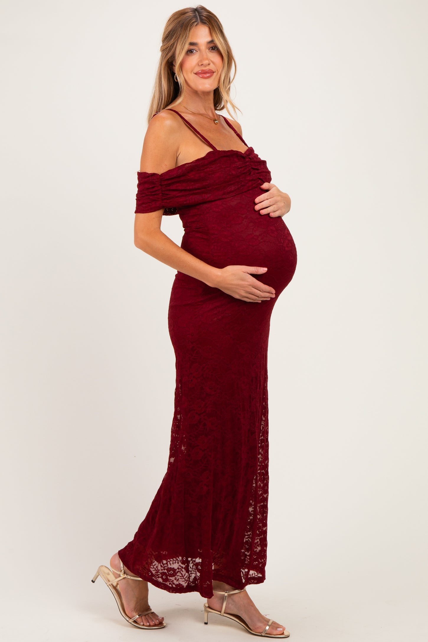 woman wearing a burgundy off-the-shoulder lace maternity dress and holding her baby bump