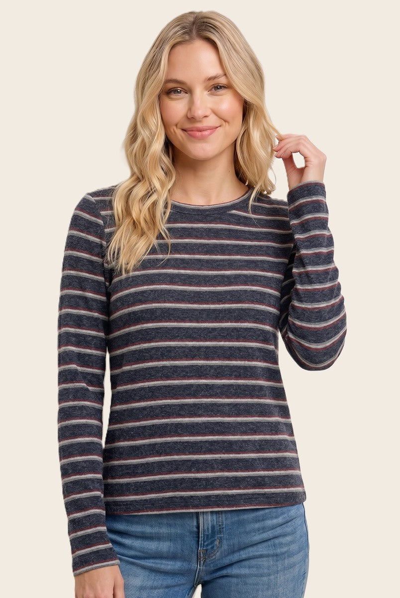 woman wearing a navy striped long sleeve top with pink and white lines, smiling and touching her hair