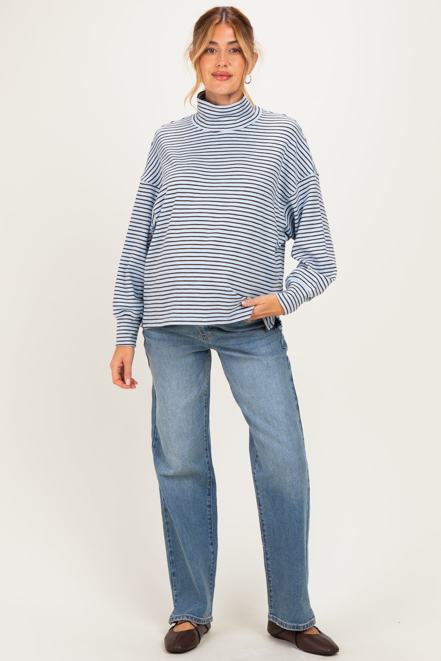 woman wearing a blue and white striped maternity sweater with a high neck and relaxed fit, paired with light jeans