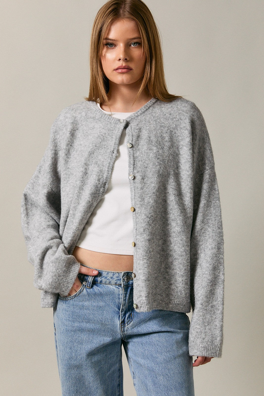 woman wearing a grey button-up cardigan over a white top, paired with blue high-waisted jeans