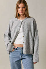 woman wearing a grey button-up cardigan over a white top, paired with blue high-waisted jeans