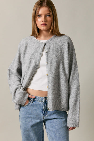 woman wearing a grey button-up cardigan over a white top, paired with blue high-waisted jeans