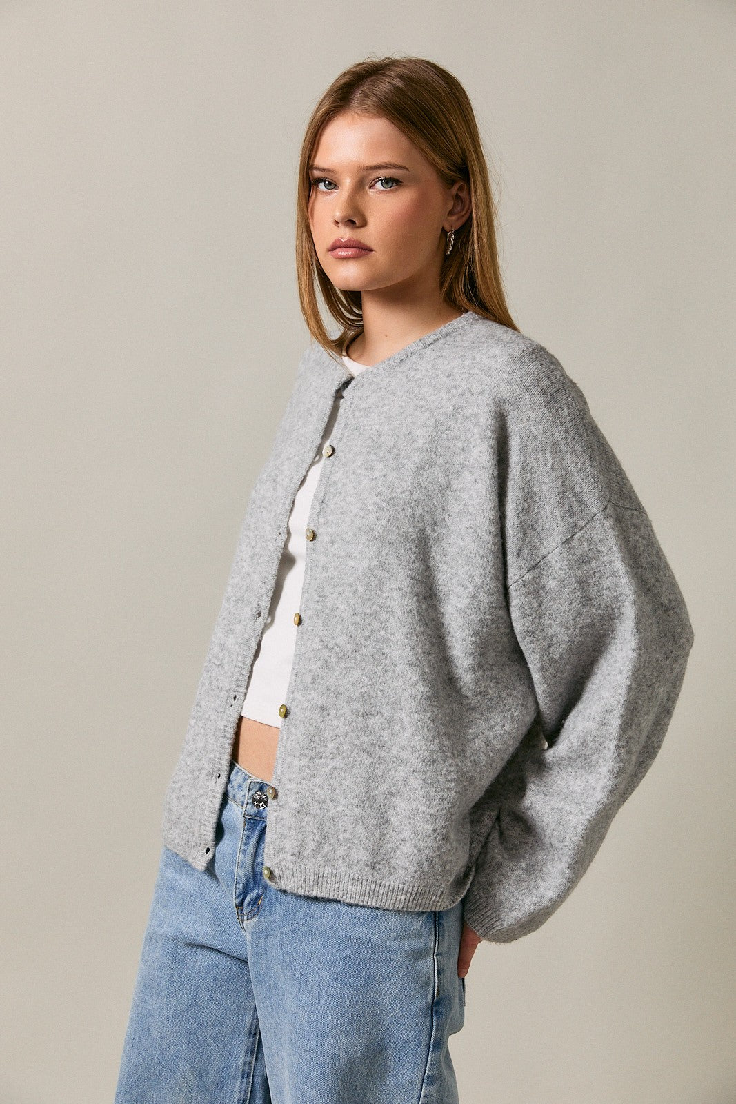 woman wearing a gray oversized cardigan with buttons and loose sleeves, paired with a white top and blue jeans