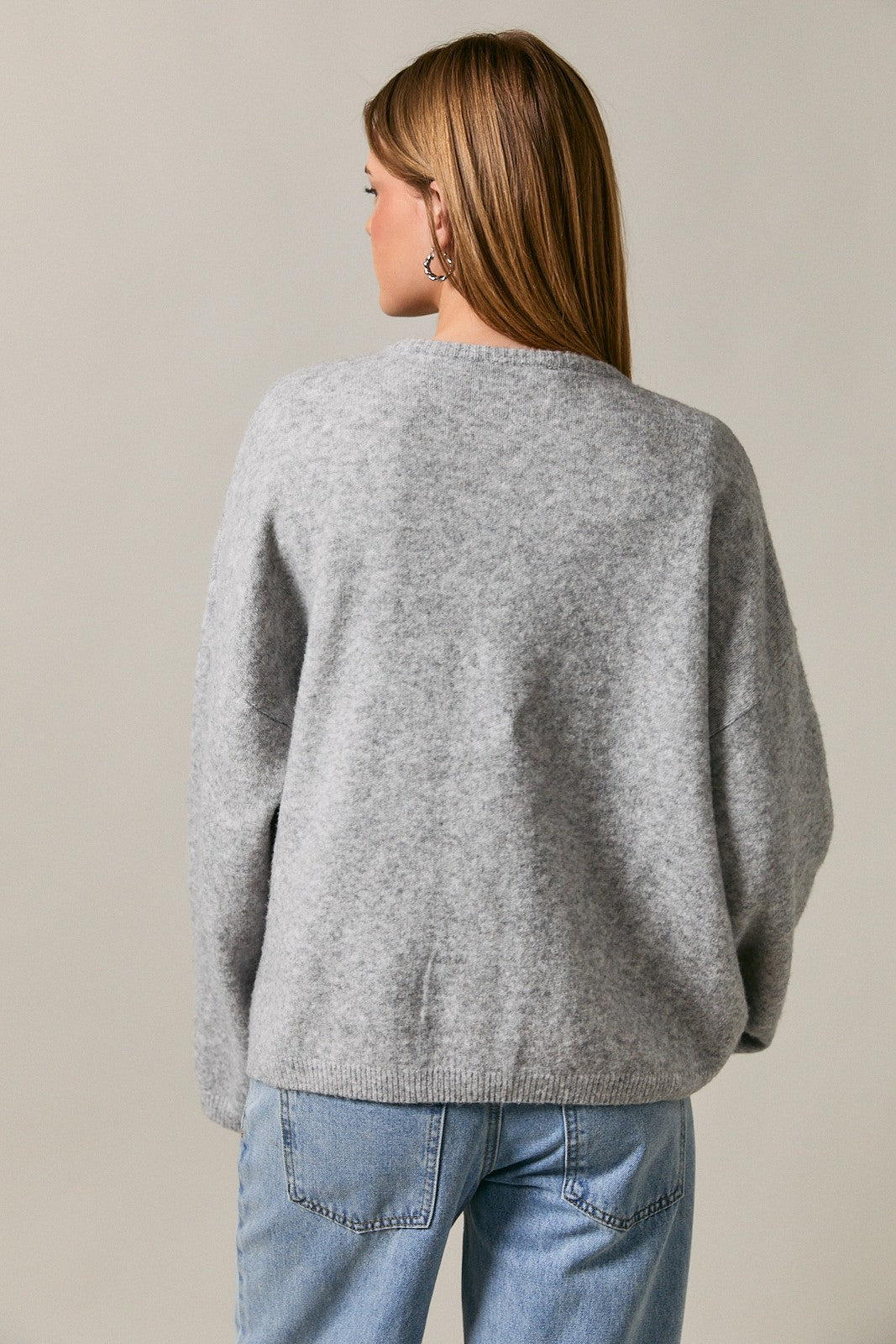 woman wearing a grey oversized knit sweater with a relaxed fit and back view, paired with light blue jeans