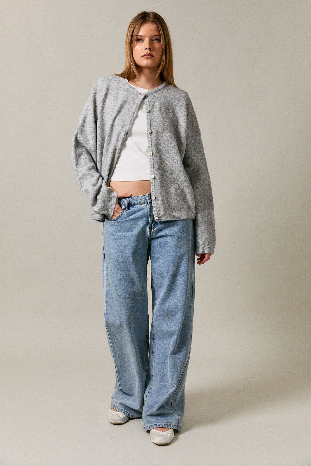 woman wearing a grey oversized cardigan over a white crop top and light blue wide-leg jeans