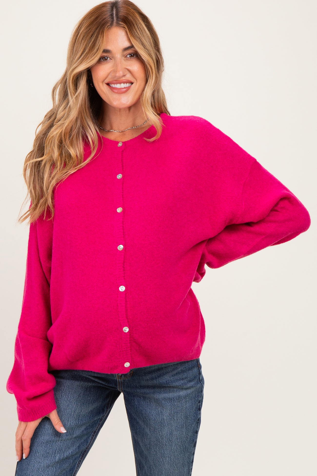 woman wearing a bright pink maternity cardigan with buttons and relaxed fit, paired with blue jeans