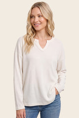 woman wearing a light cream long sleeve ribbed top with a v-neckline and relaxed fit, smiling and posing casually
