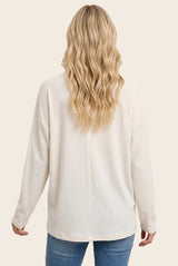 woman wearing a cream long sleeve ribbed top, viewed from the back, with wavy blonde hair and blue jeans
