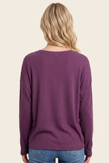 woman wearing a purple ribbed long sleeve top with a relaxed fit and scoop neckline, viewed from the back
